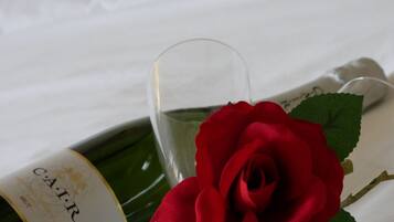 A bottle of wine, a glass, and a red rose on a bed.