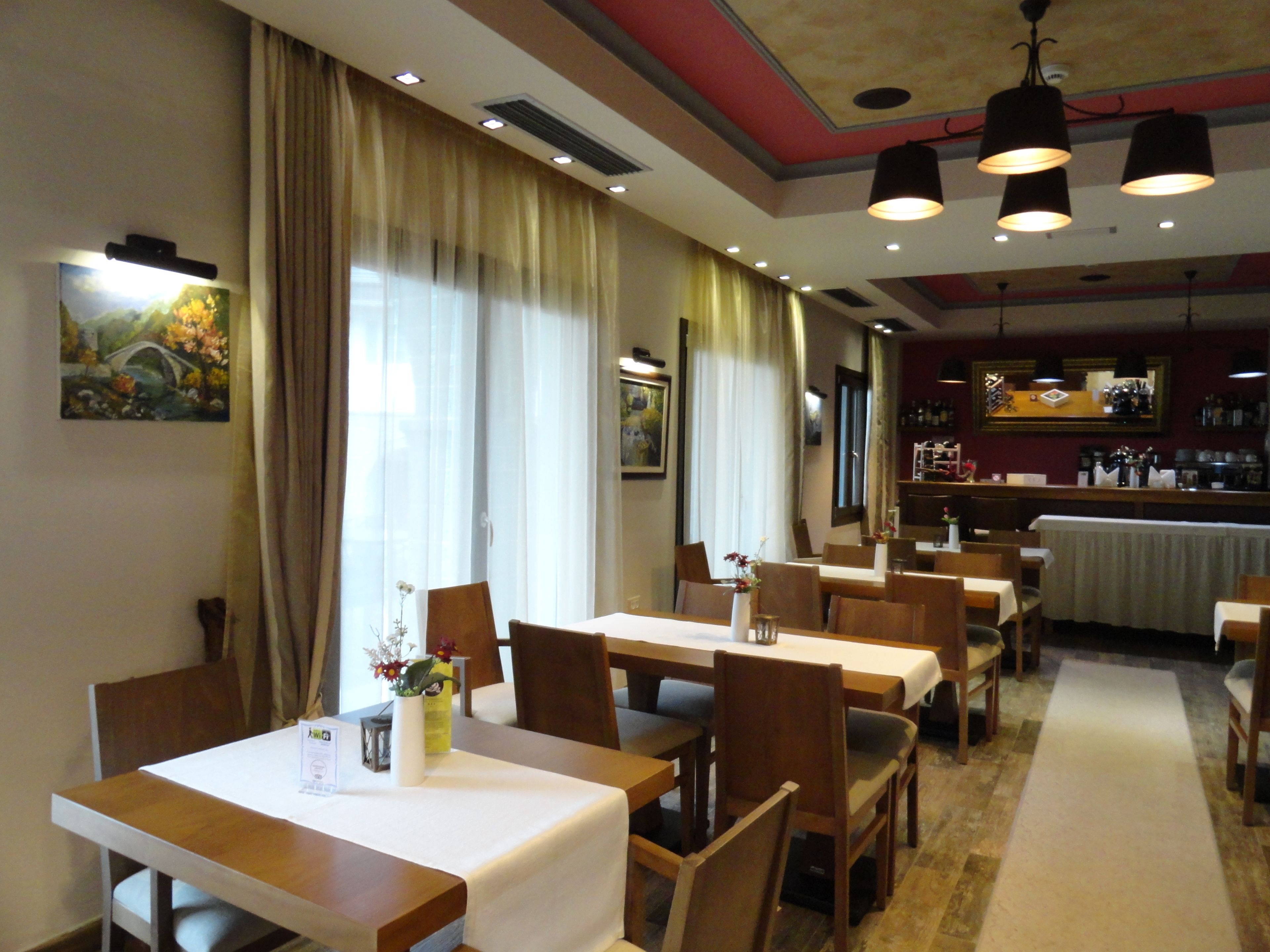 En restaurang med träbord och stolar, en bardisk och en tavla på väggen.