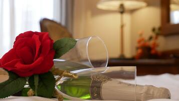 A champagne bottle and a red rose on a bed.