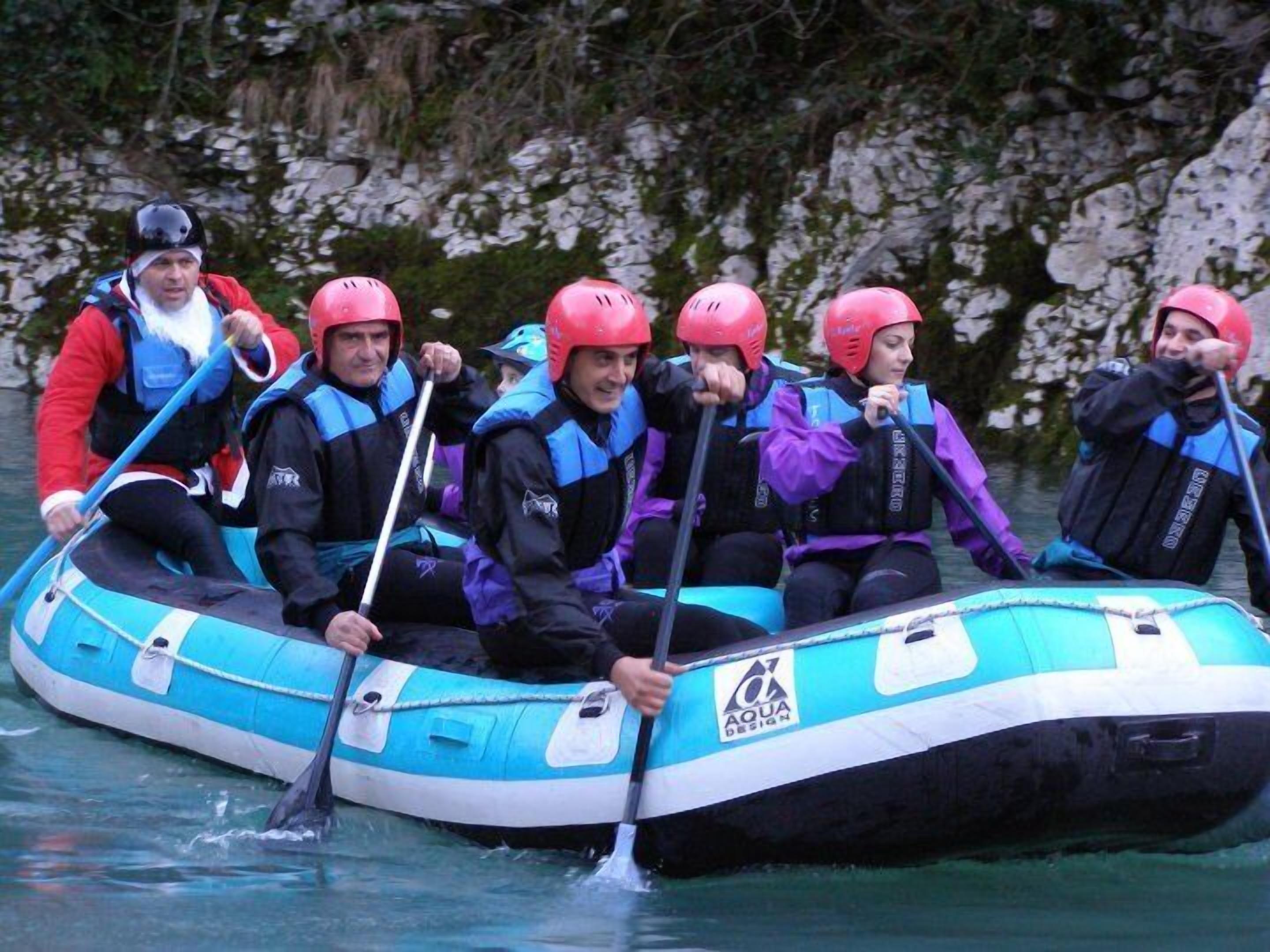 Un gruppo di persone su un’imbarcazione gonfiabile blu e bianca, con un logo, pagaia sull'acqua.