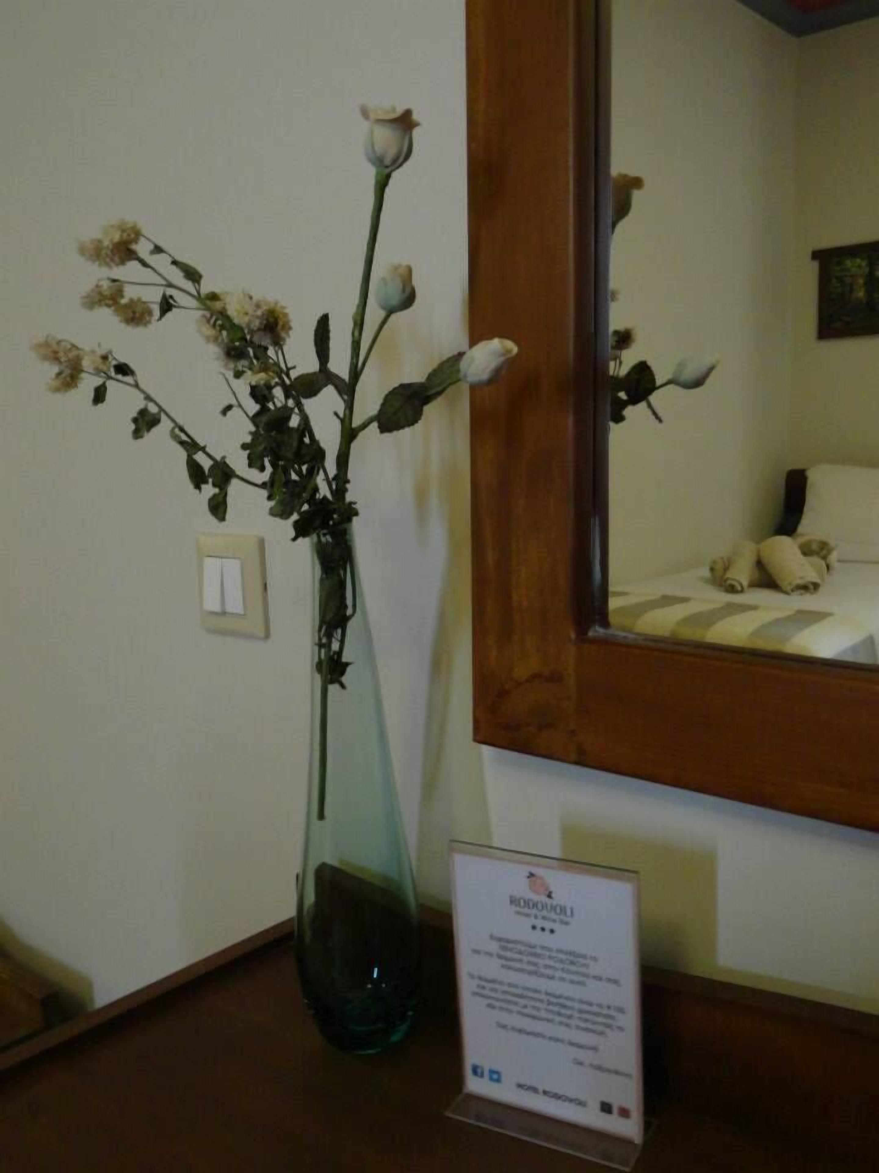 A room with a large mirror, a vase with flowers, and a sign on the wall.