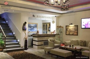 Zona de recepción de hotel con escalera, mostrador de recepción y área de estar.
