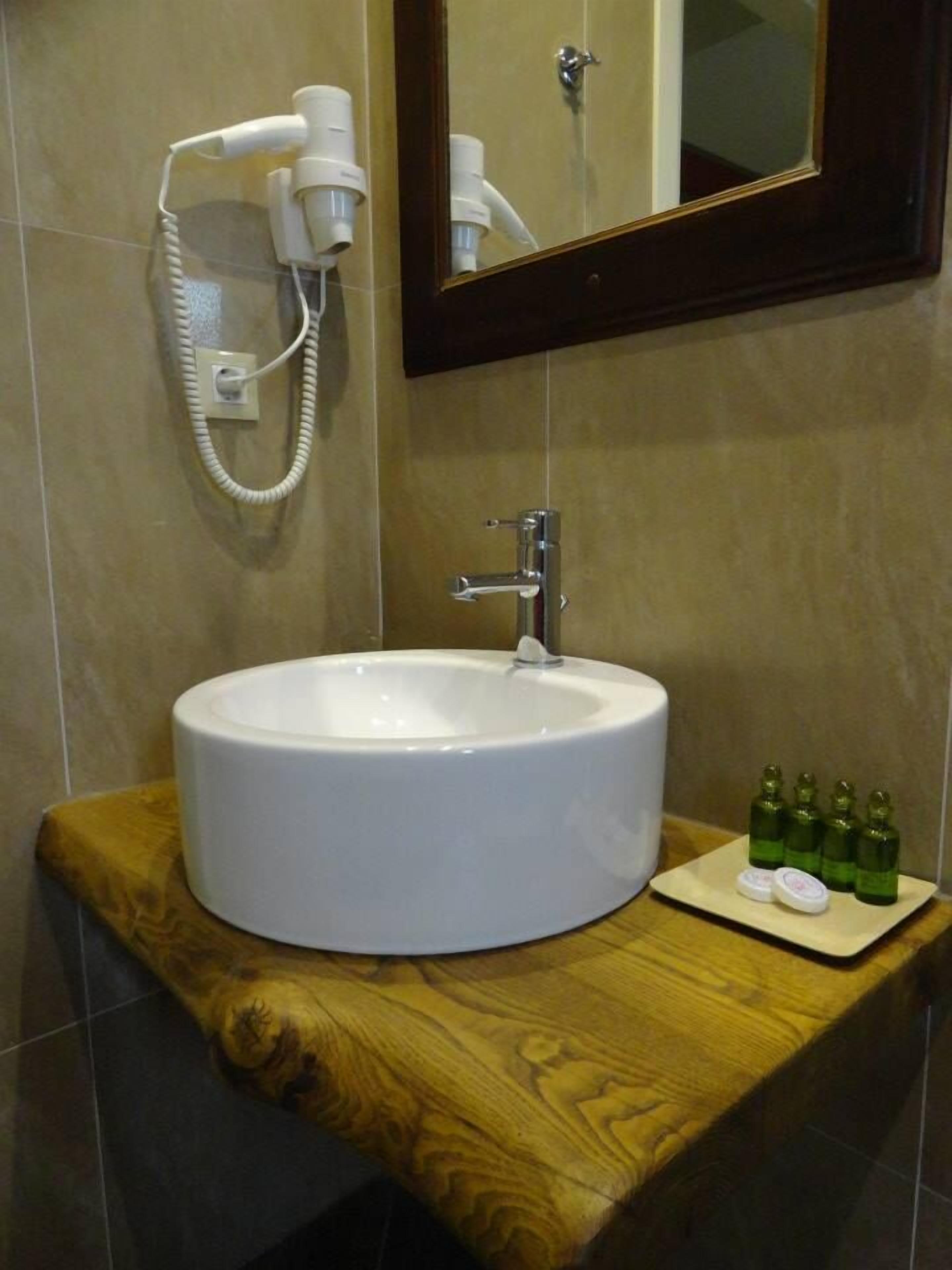 A bathroom with a round white sink, a mirror, and a hairdryer mounted on the wall.