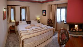 A hotel room with a large bed, a bedside table with a lamp, a chair, a fireplace, and a painting on the wall.
