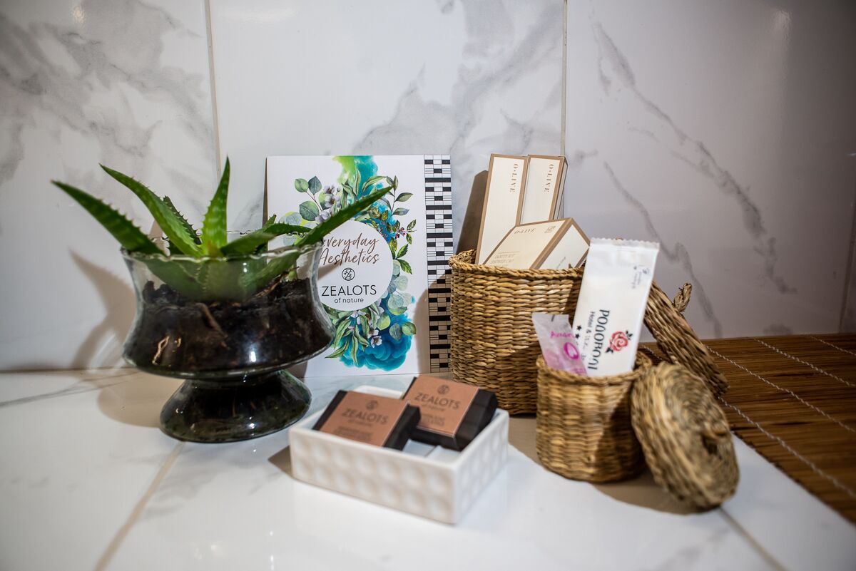 Pared de baldosas de mármol con una planta de aloe vera en maceta, un cuaderno y una cesta de mimbre con productos para el cuidado de la piel.