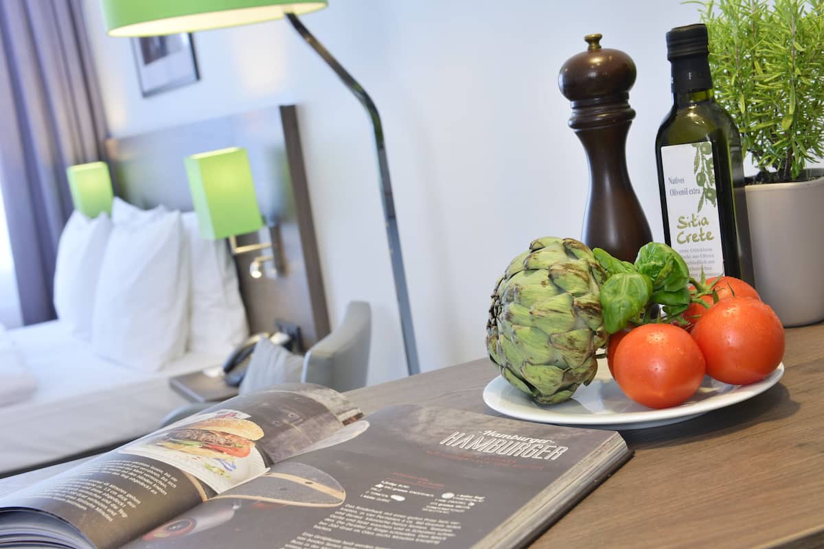 Une table avec un magazine ouvert, une assiette contenant des artichauts et des tomates, un moulin à poivre et une bouteille d’huile d’olive.