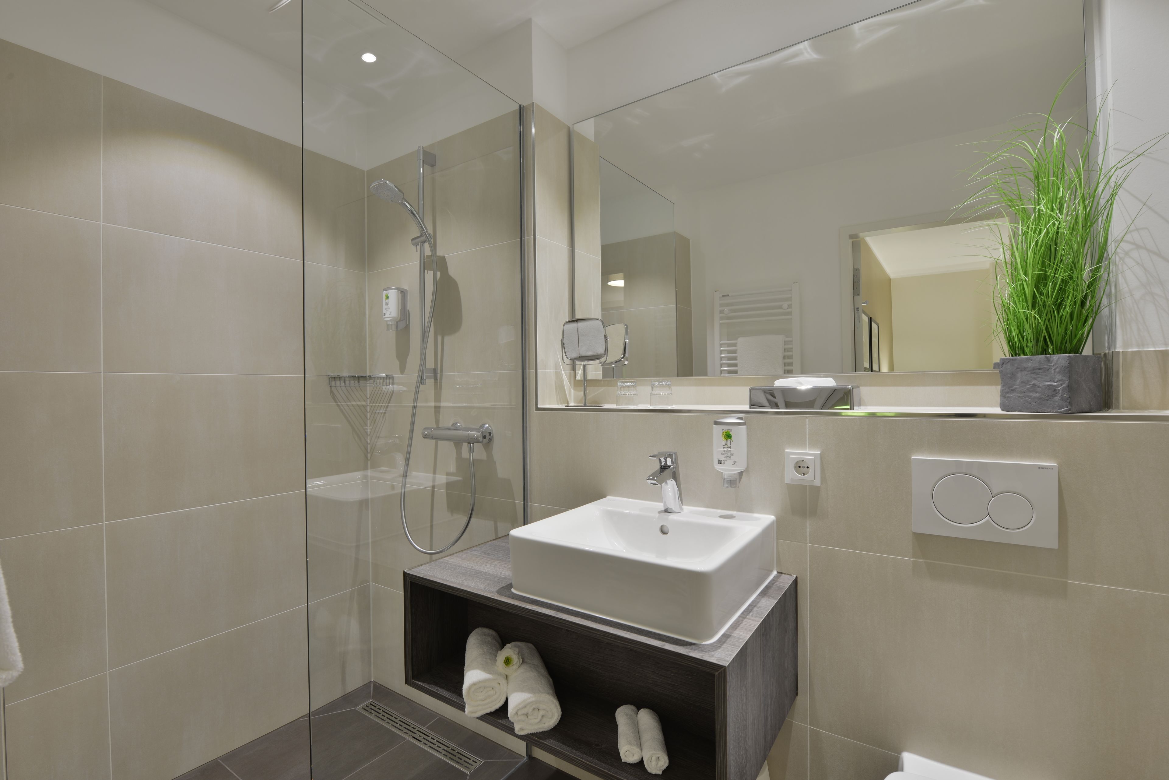 Ein modernes Badezimmer mit einer gläsernen Dusche, einem weißen Waschbecken und einer eingebauten Ablage mit Handtüchern.