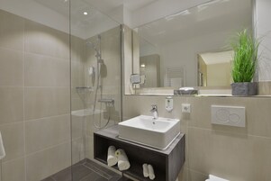 Ein modernes Badezimmer mit einer gläsernen Dusche, einem weißen Waschbecken und einer eingebauten Ablage mit Handtüchern.