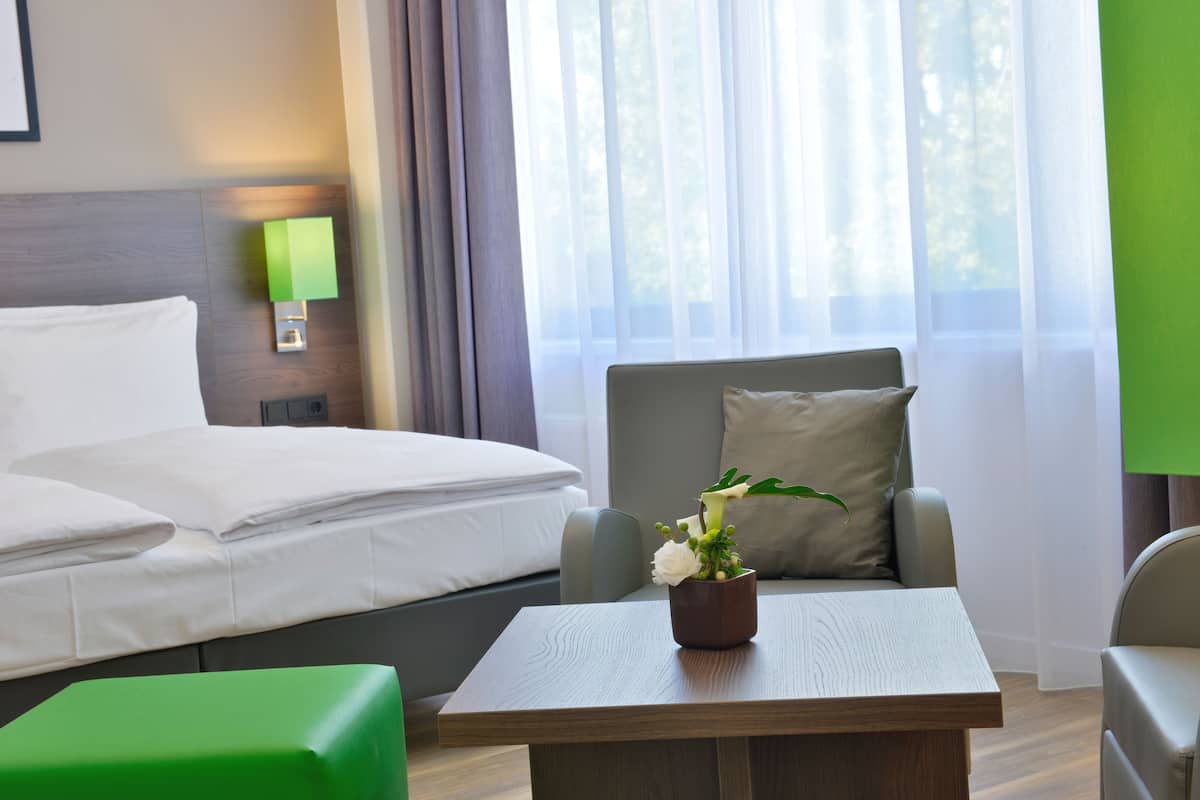 Une chambre d’hôtel avec un lit, une chaise, une petite table et une fenêtre avec des rideaux.