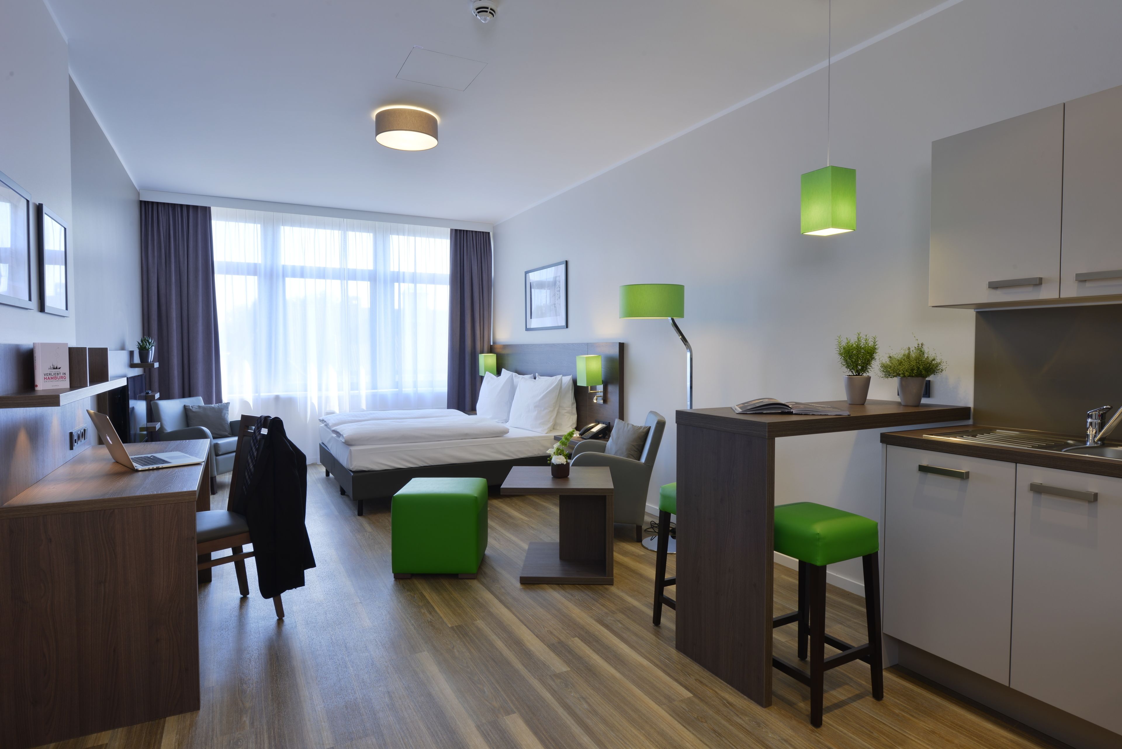 Une chambre d’hôtel moderne équipée d’un lit, d’un bureau, d’une kitchenette et d’un coin salon.