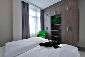 A hotel room with two beds, a green chair, and a TV on a wooden cabinet. - appartello - smarttime living Hamburg (Hamburg)