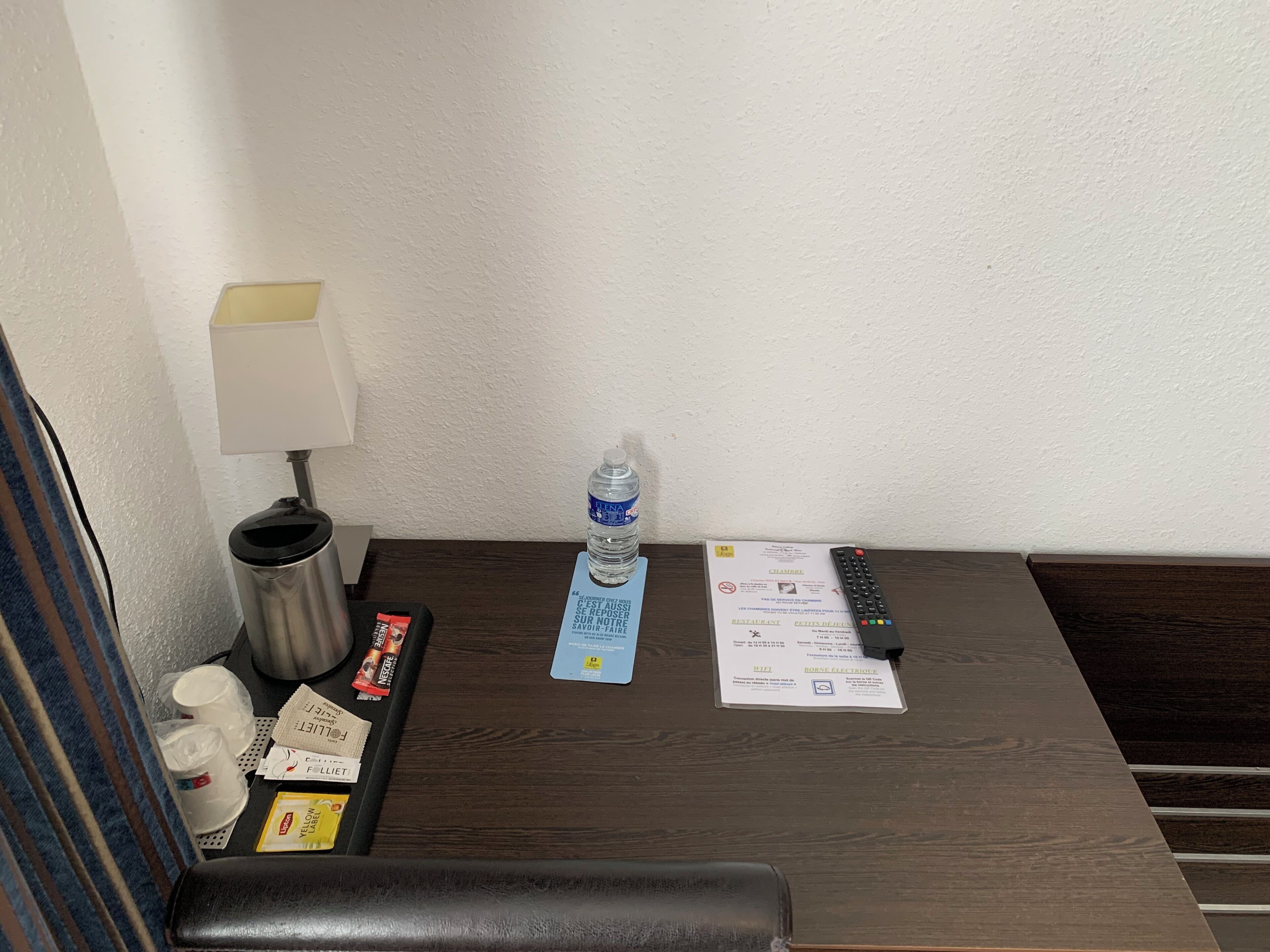Una habitación de hotel con un escritorio de madera, una botella de agua, un mando a distancia y un menú.