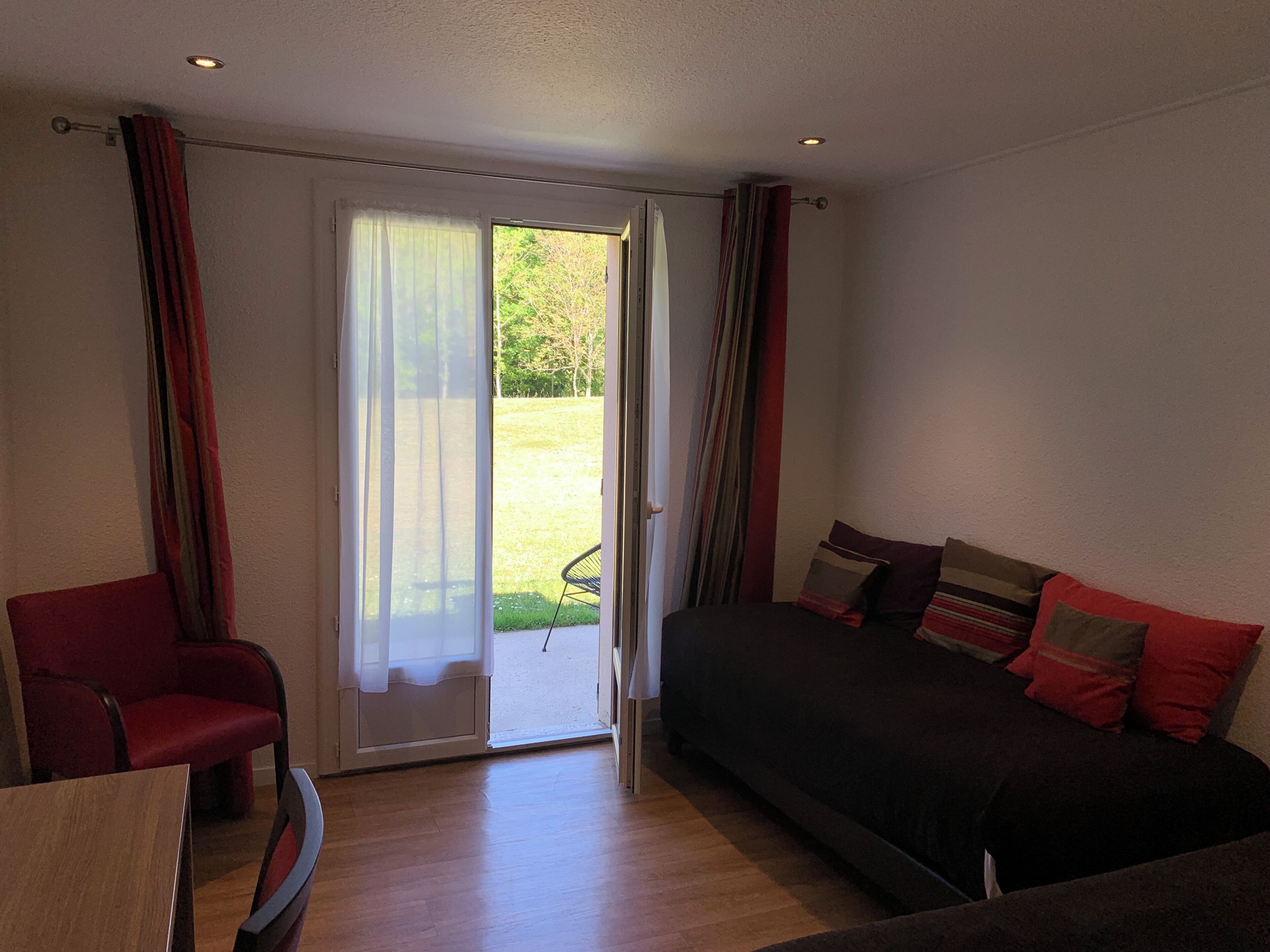 A room with a bed, a chair, a table, and a sliding glass door leading to a garden.
