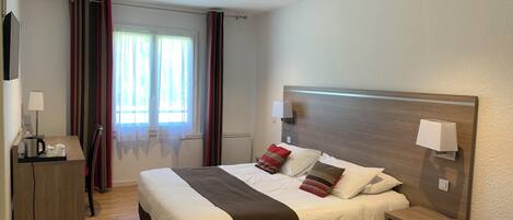 Una habitación de hotel con cama, mesita de noche, lámpara y escritorio con lámpara.