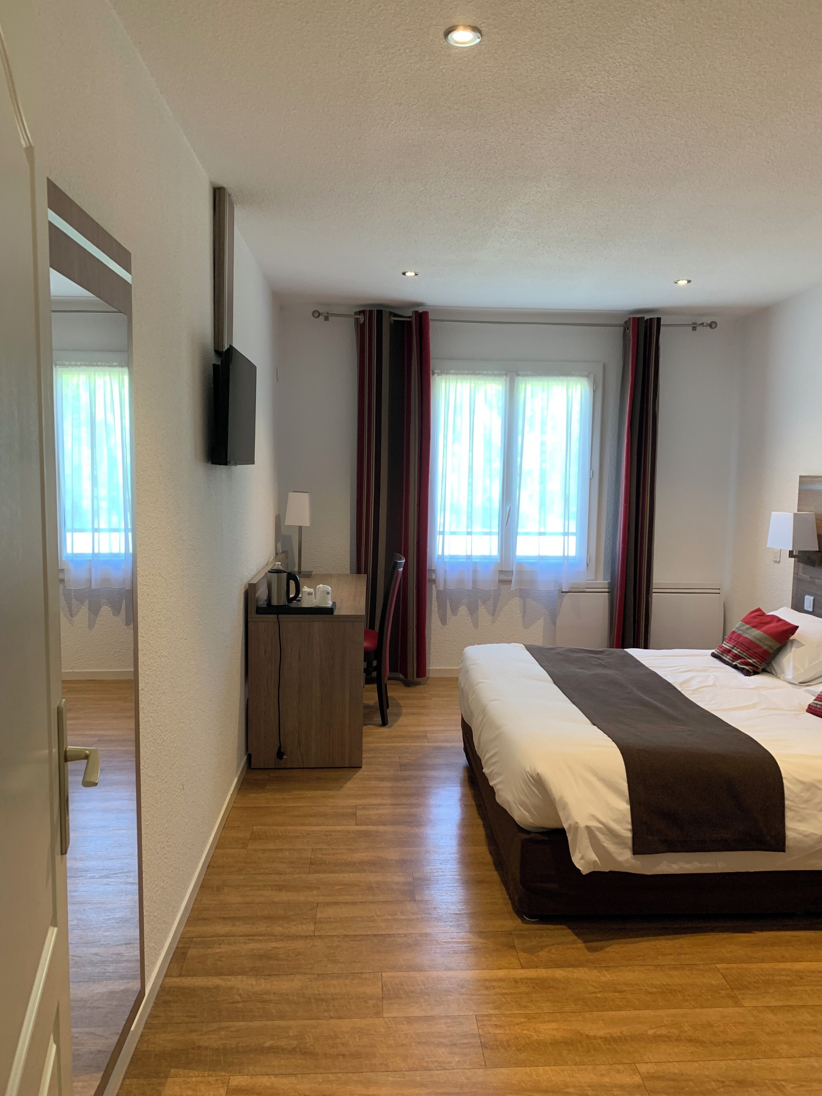 Une chambre d’hôtel avec un lit, un bureau, une chaise, une télévision et une fenêtre avec des rideaux.