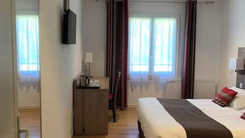 Une chambre d’hôtel avec un lit, un bureau, une chaise, une télévision et une fenêtre avec des rideaux.
