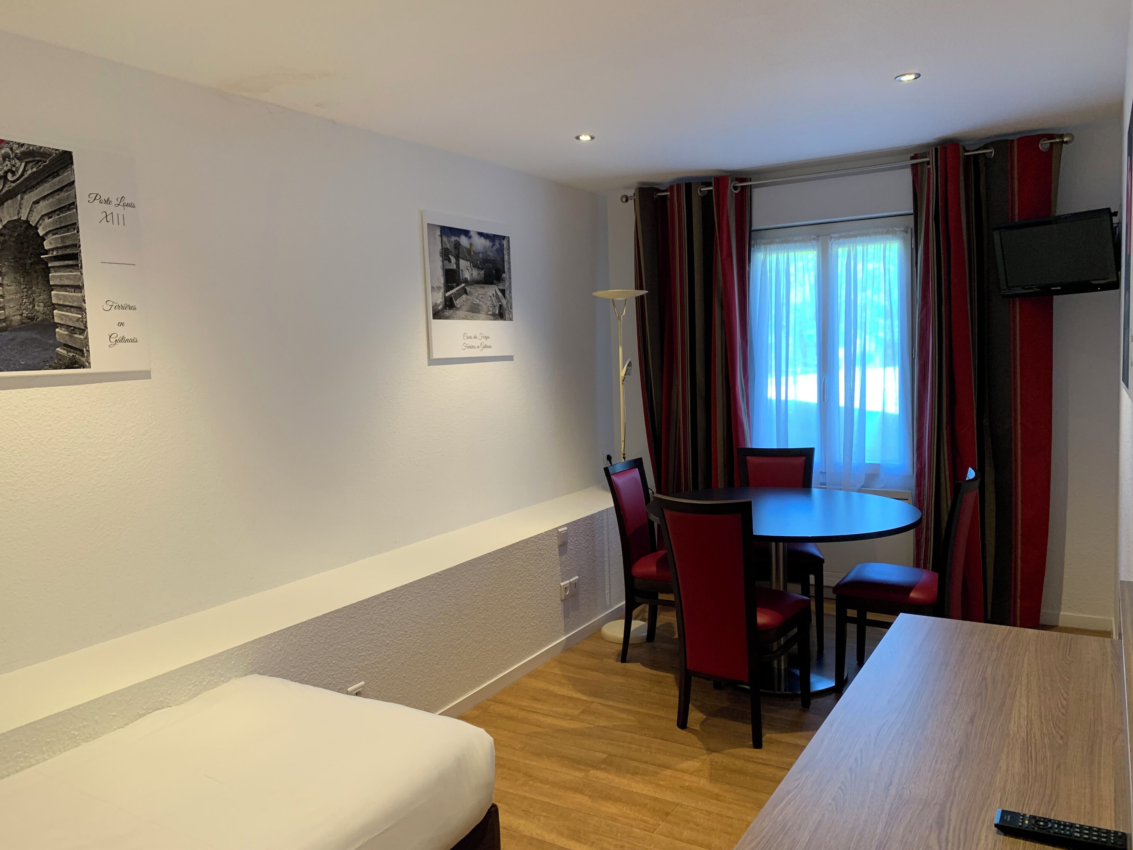 Une chambre d’hôtel avec un lit, une table à manger avec des chaises, une télévision et une fenêtre avec des rideaux.