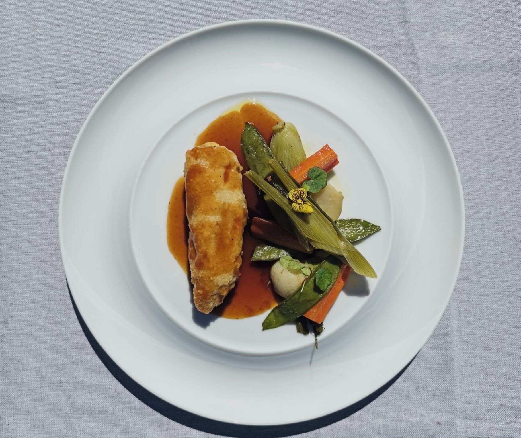A white plate with a piece of breaded fish, vegetables, and a sauce.