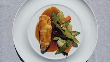 Ein weißer Teller mit paniertem Fisch, Gemüse und Soße.