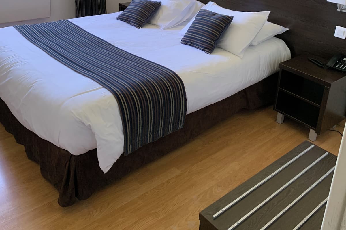 A neatly made bed with white linens and striped pillows, a bedside table with a lamp, and a window with curtains.