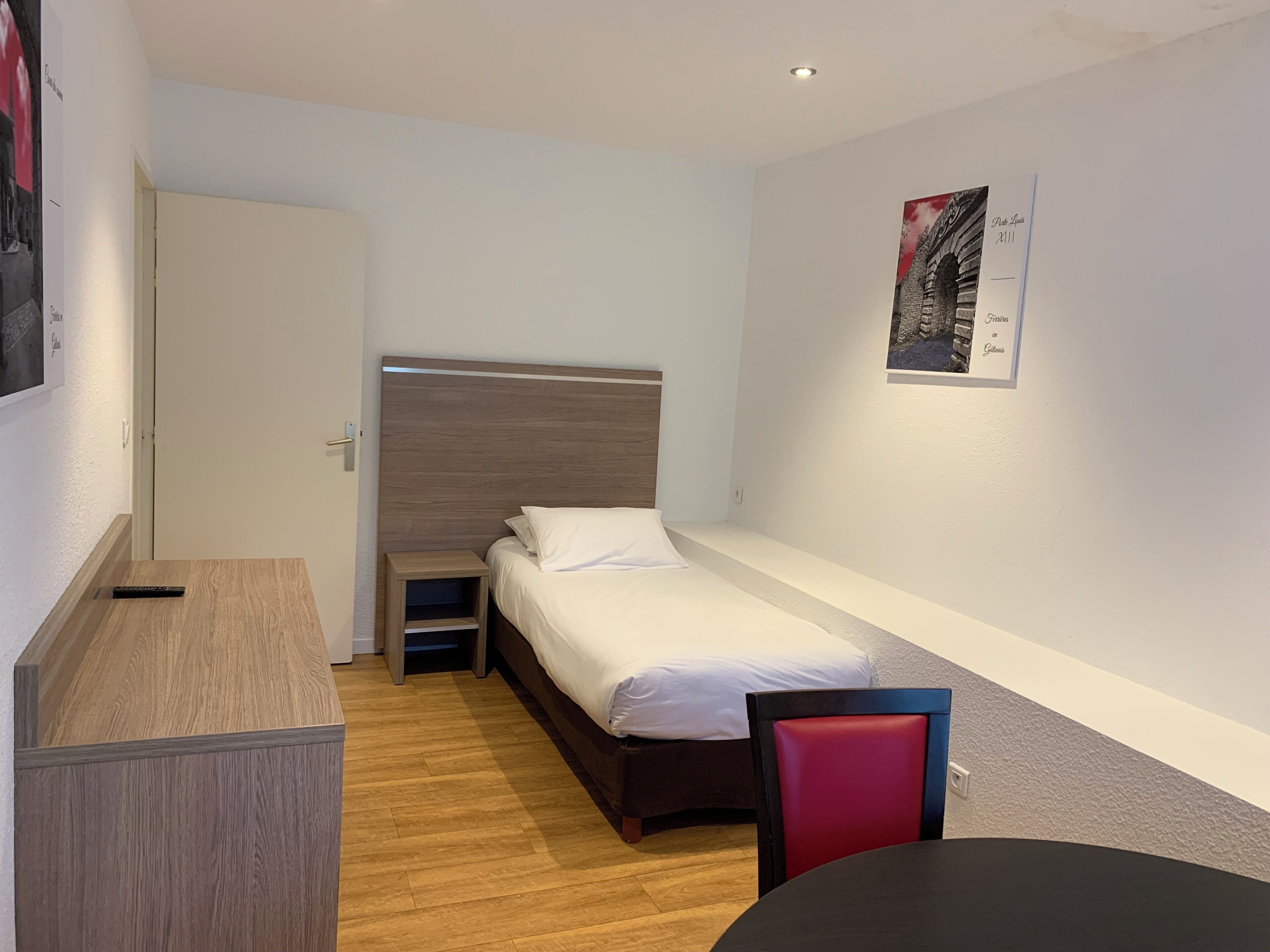 Una habitación pequeña y ordenada con cama, escritorio, silla y una mesita.