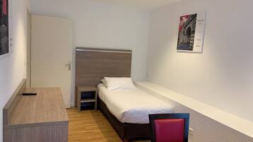 Een kleine, netjes ingerichte kamer met een bed, een bureau, een stoel en een tafeltje.