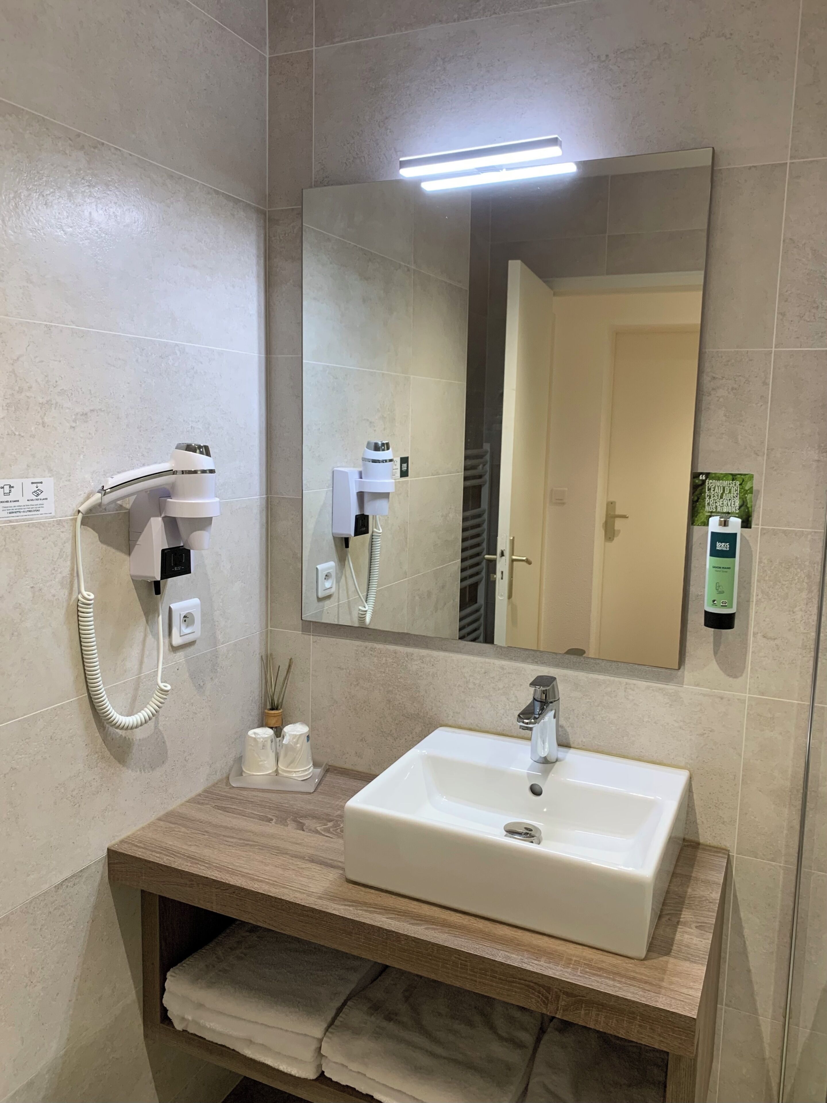 Une salle de bain avec un lavabo blanc, un miroir, un sèche-cheveux et un porte-serviettes.