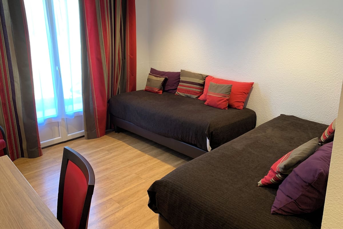 A bedroom with two beds, a chair, and a window with curtains.