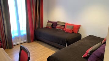 A bedroom with two beds, a chair, and a window with curtains.