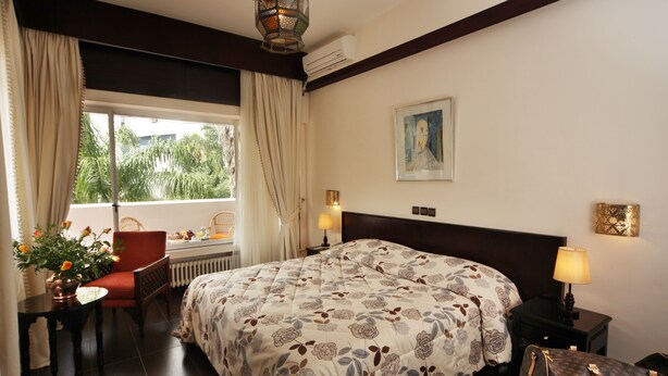 A hotel room with a large bed, a desk with a chair, a window with curtains, a lamp, and a painting on the wall.