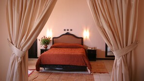 Un dormitorio con cama, cortinas, una mesita de noche, una lámpara y un aplique de pared.