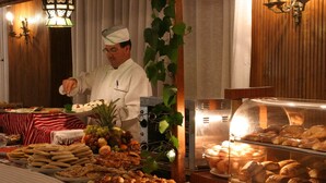 Un bufé con diversas opciones de comida, un chef y una vitrina con pasteles.