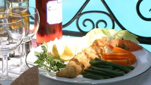 A table with a bottle of wine, glasses, and a plate of food including vegetables and bread.