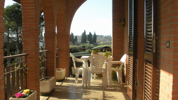 Une terrasse extérieure couverte, avec des murs en briques, des chaises en plastique blanches et des jardinières fleuries.