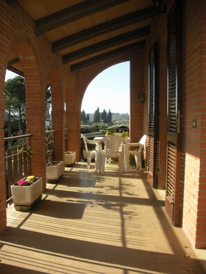 Un patio al aire libre cubierto con paredes de ladrillo, sillas de plástico blanco y macetas con flores.