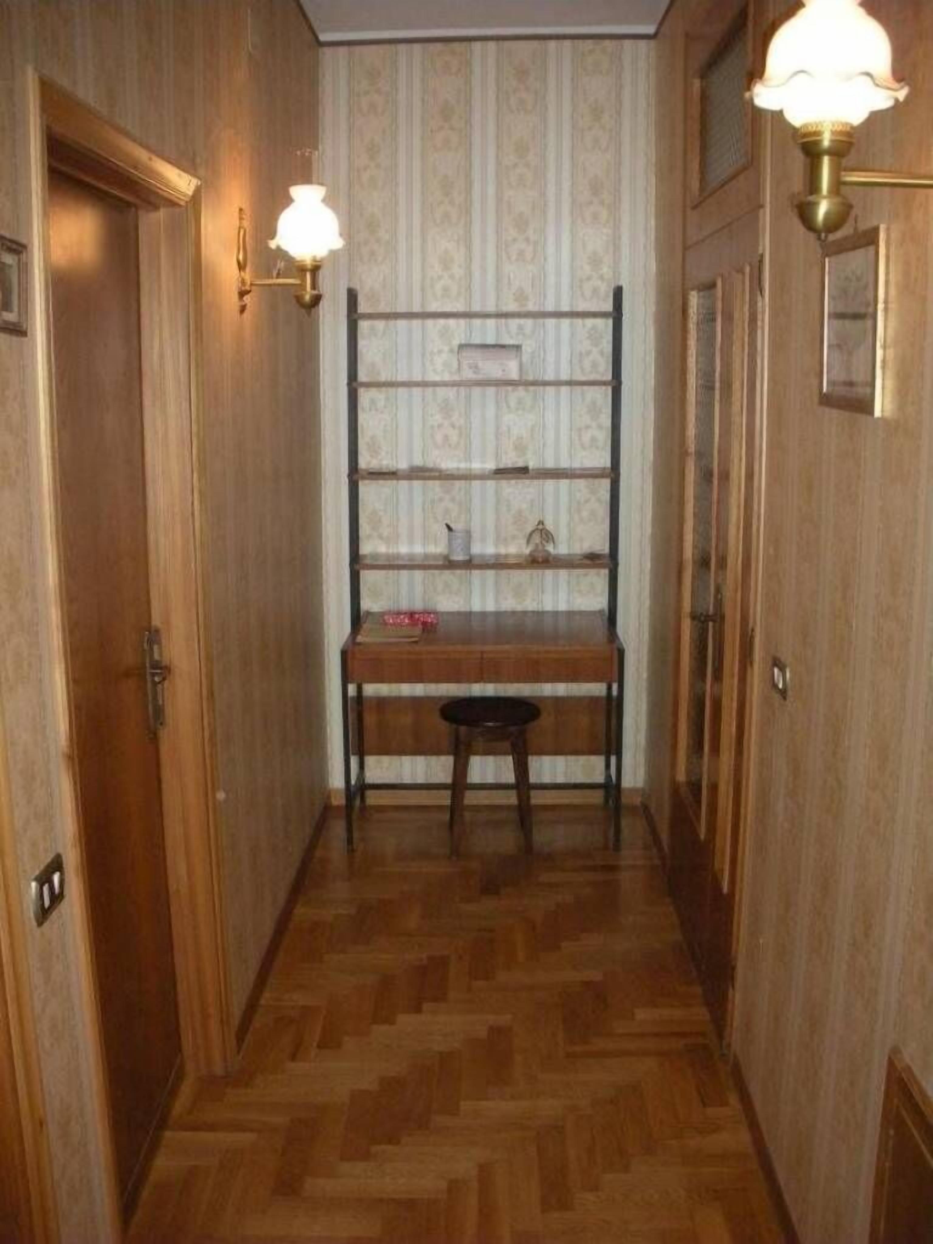 A narrow hallway with wooden flooring, a bench, and two wall-mounted lamps.