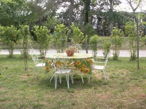 Un espace extérieur aménagé pour les repas, avec une table ronde et des chaises en métal blanc, entouré de petits arbres et d’herbe.