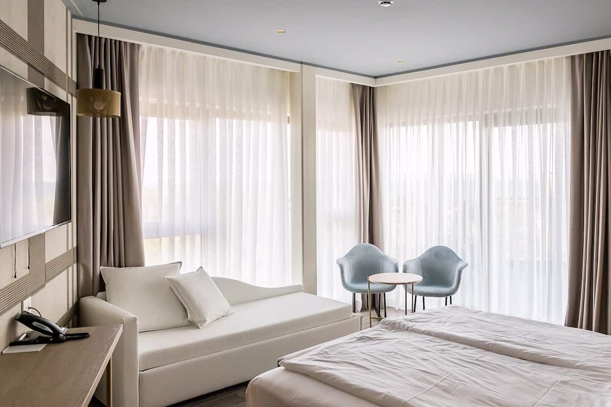 A modern hotel room with a bed, a sofa, a desk, and a TV.