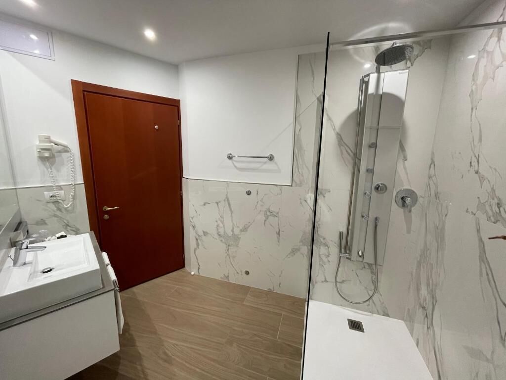 Ein modernes Badezimmer mit einer Duschkabine aus Glas, einer Holztür und einer Wand mit Marmorplatten.