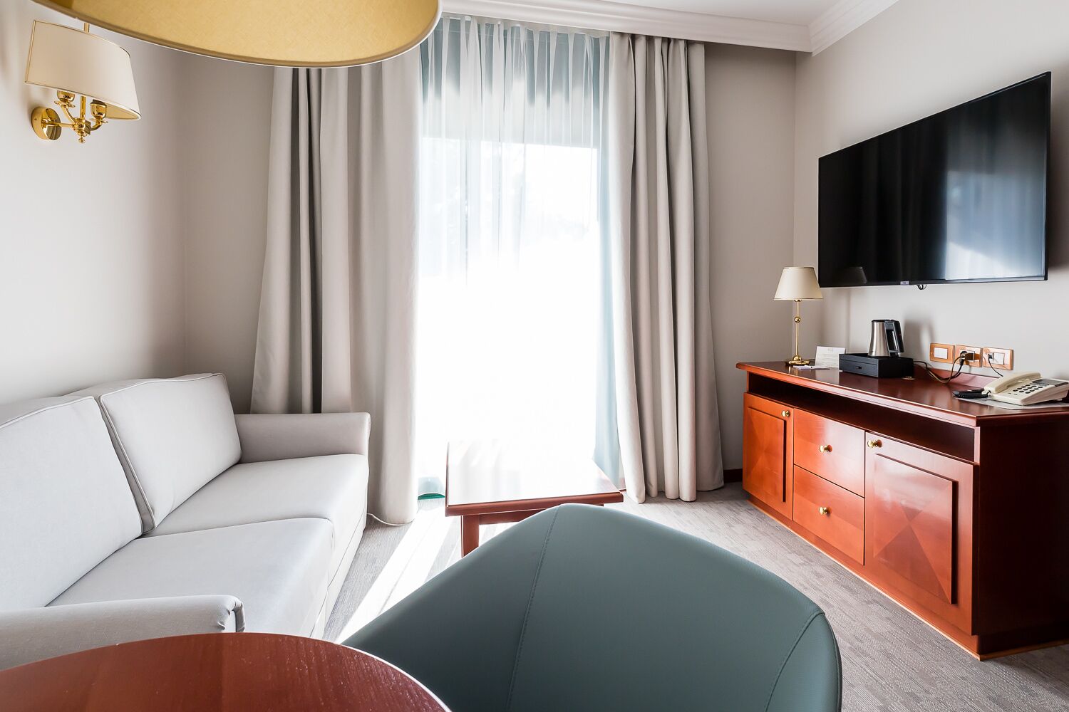 Habitación de hotel con sofá, escritorio con teléfono, cafetera y televisión montada en la pared.