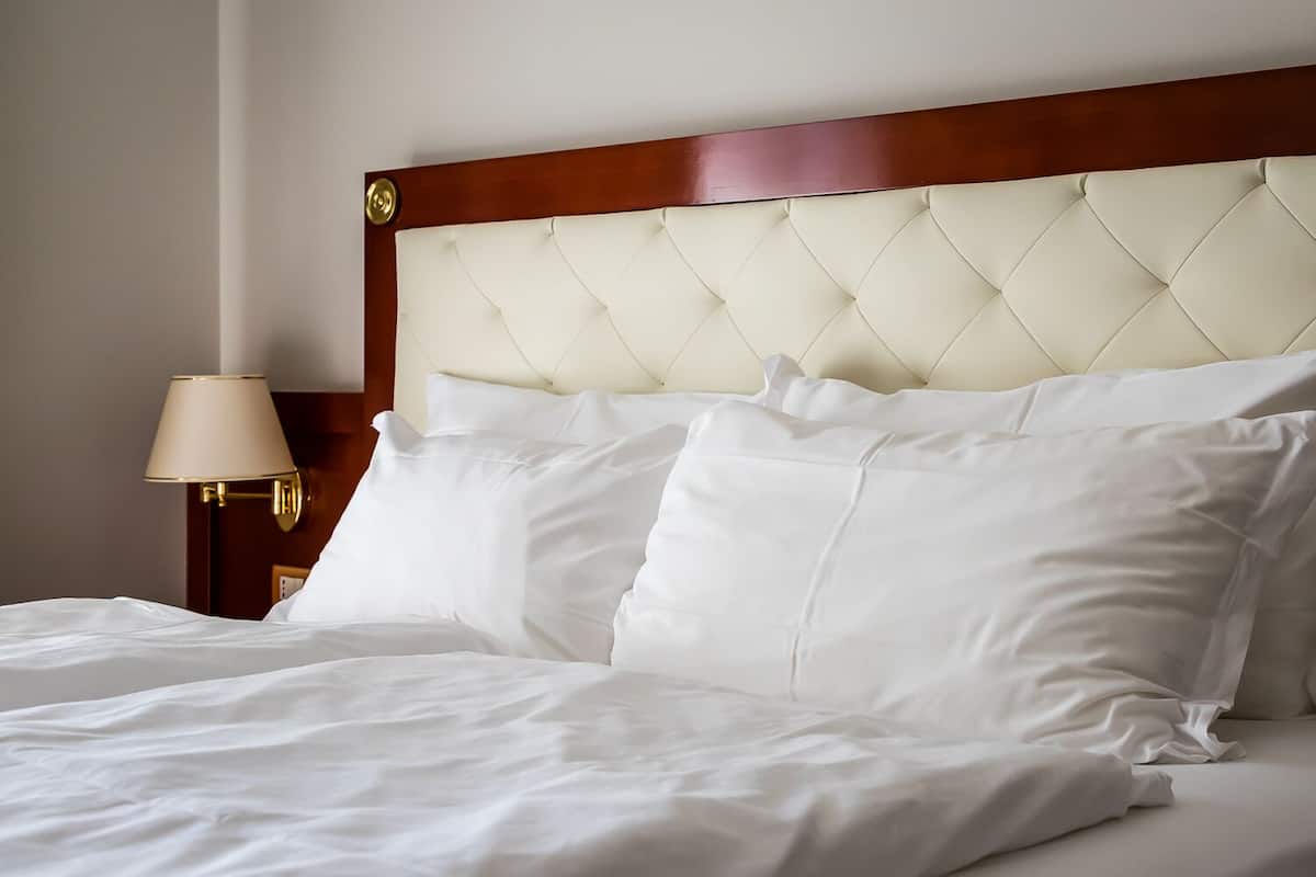 A neatly made bed with white linens and a tufted headboard.