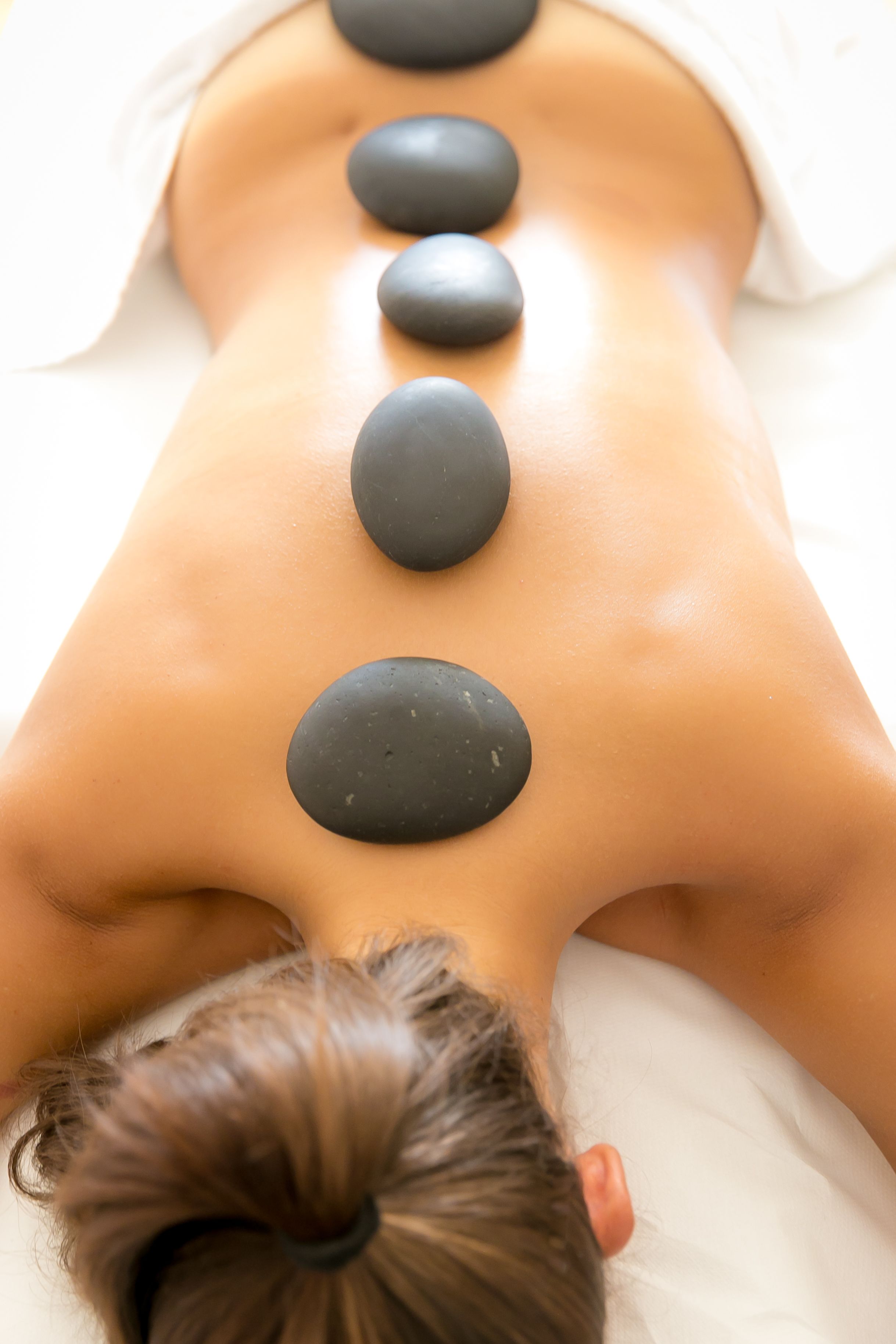 En person modtager en rygmassage med sten placeret langs rygsøjlen.