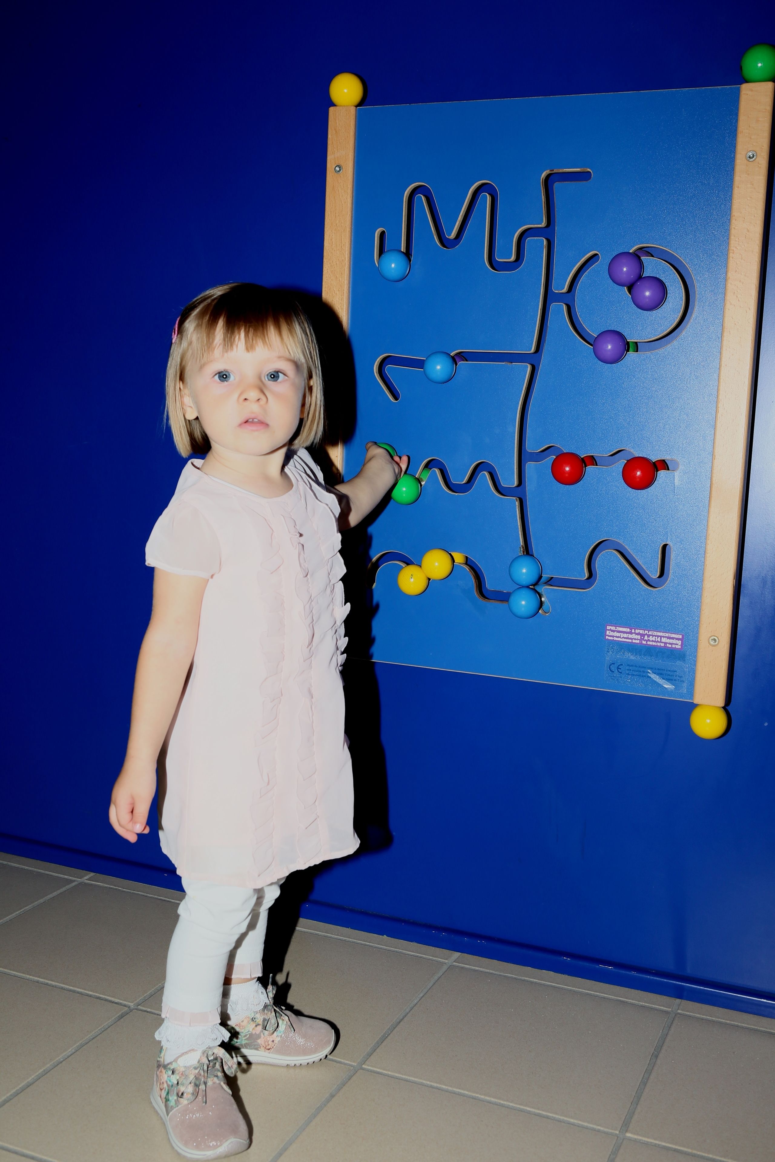 Ein Kind steht neben einer blauen Wand mit einer Holzplatte, die ein Labyrinth zeigt.