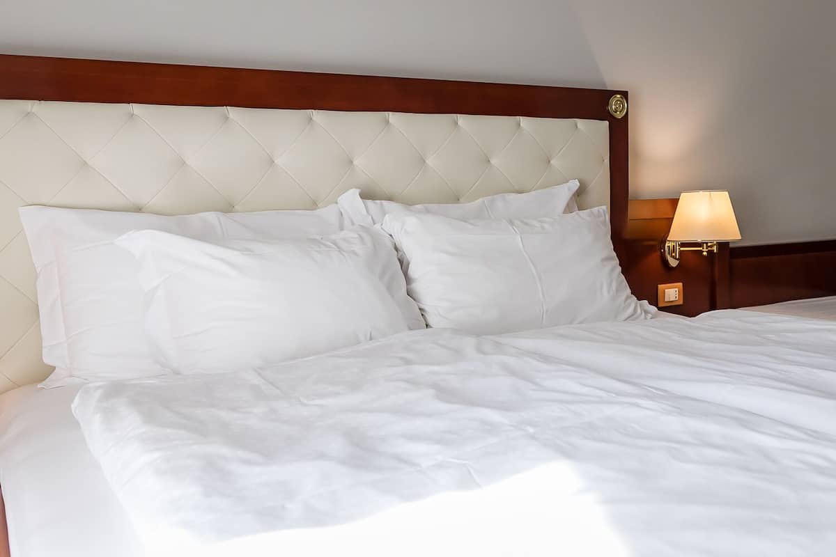 A neatly made bed with white linens and a tufted headboard.