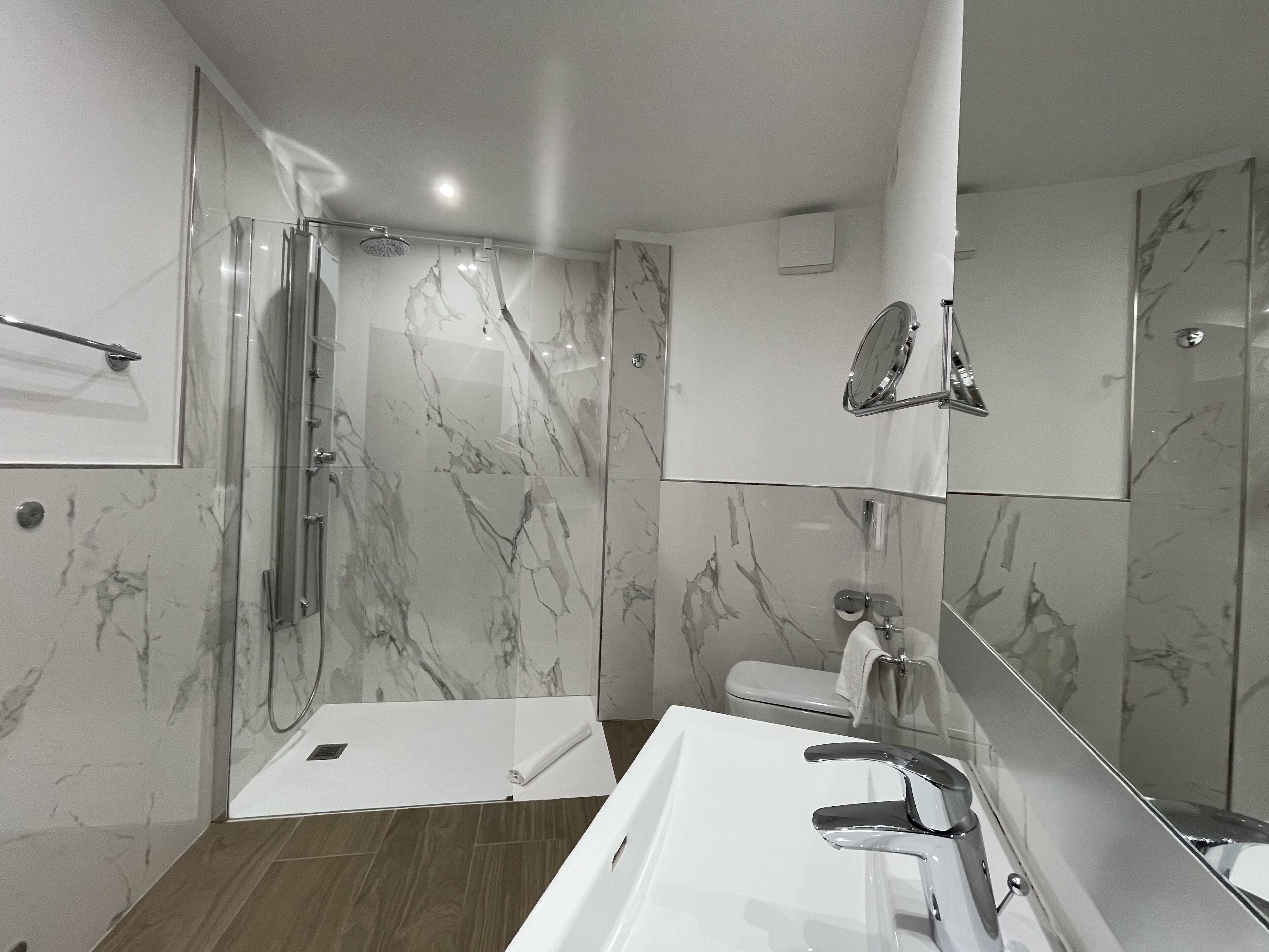 Une salle de bain moderne avec une douche à l’italienne en verre, un lavabo blanc et un grand miroir.