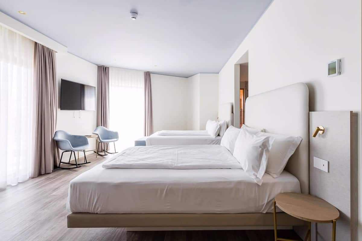 A modern hotel room with two beds, a TV, a desk, and a chair.
