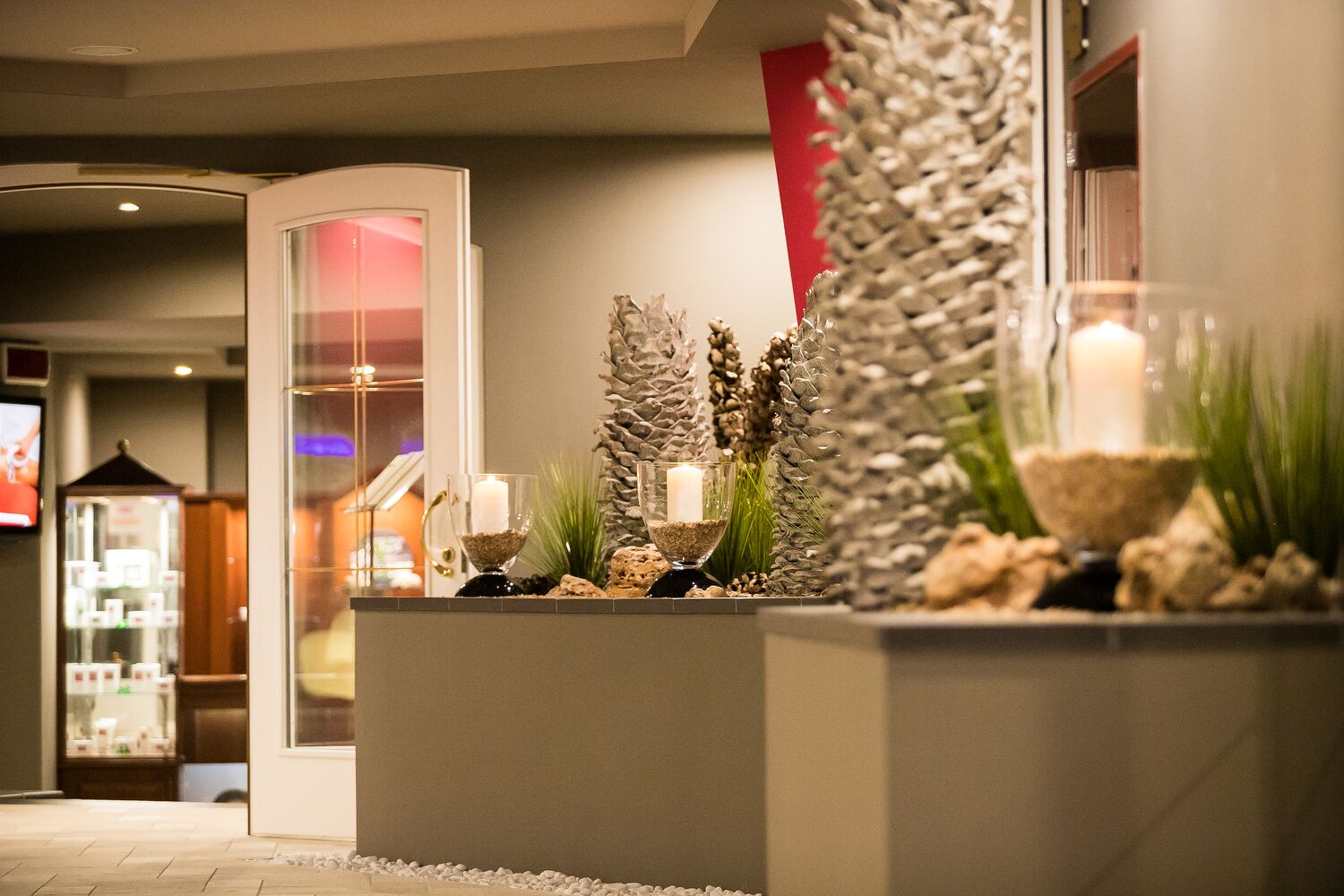 A reception area with a modern design, featuring a reception desk, a glass partition, and decorative elements like candles and plants.