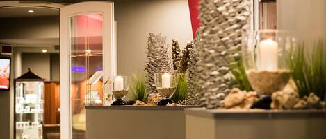 A reception area with a modern design, featuring a reception desk, a glass partition, and decorative elements like candles and plants.