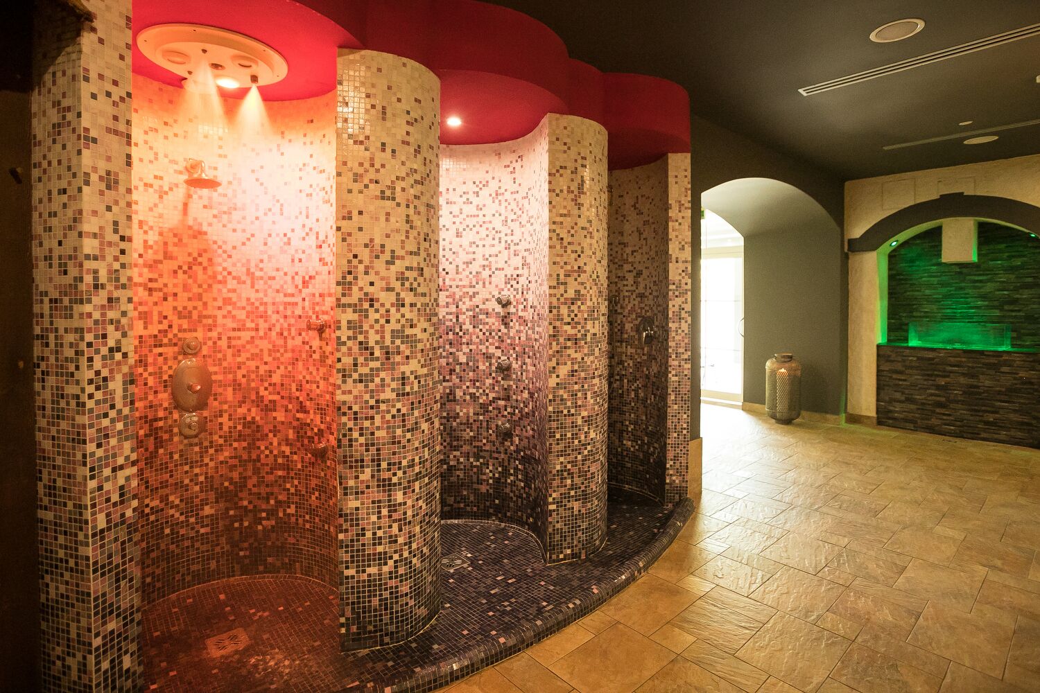 Een betegelde muur met een mozaïekpatroon, een rood plafond en een muur op de achtergrond verlicht met groen licht.