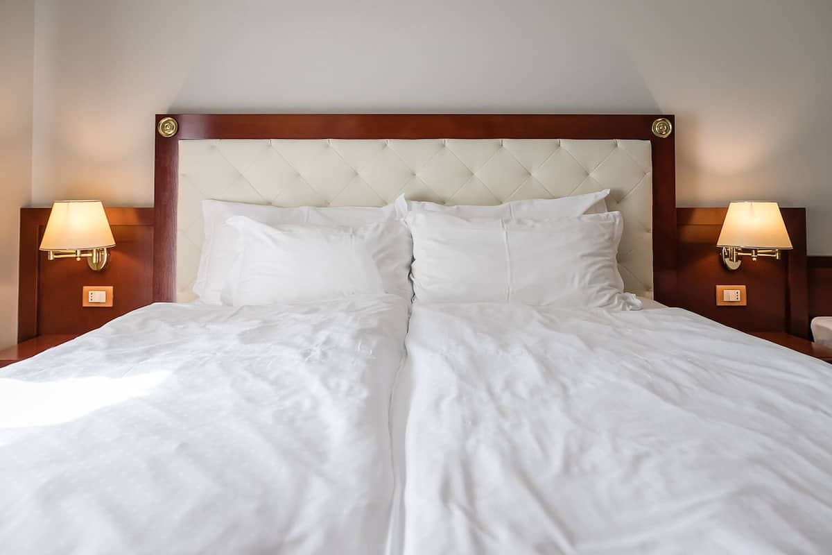 A large bed with a tufted headboard, two bedside lamps, and white bedding.